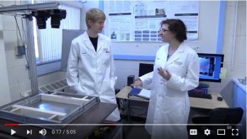 Scientific lab with two scientists in white lab coats facing each other talking, 3/4 view towards camera. Male identified scientist on left, female identified scientist on right.