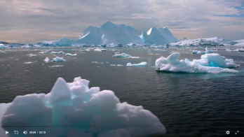 Gravel-strewn shoreline on edge of ice-covered sea, with winter-bundled person standing in middle-distance, looking away from the viewer.  Image credit: PBS