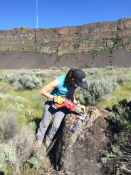 Karin Legnick in steep sided open canyon using a power tool on a boulder.